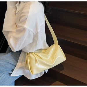 Detailansicht der hellgelben glänzenden Leder-Schultertasche, getragen von einem Model