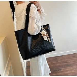 Detail of a large black tote bag with H.SHAN embossing and a white plush bear charm