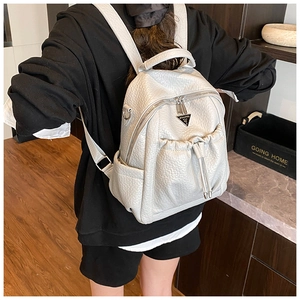 Rear view of model wearing a textured white faux leather backpack with metal logo