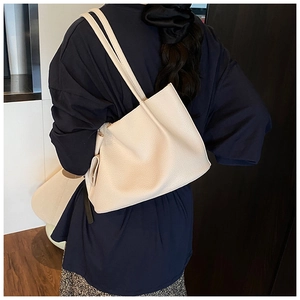 Rear view of beige lychee texture tote bag worn over shoulder on dark blue outfit