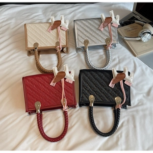 Quatre sacs à main tressés en beige, argent, rouge et noir avec breloques ailes