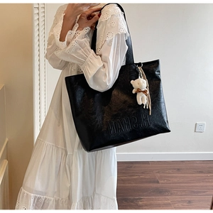 Detail of black tote bag with H.SHAN embossing and soft plush bear charm decoration