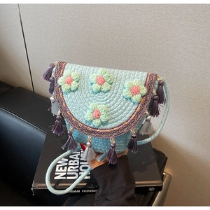 Detail of light blue hand-woven crossbody bag with floral accents and fringe trim