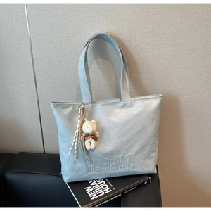 Detail of light blue tote bag with embossed H. SHAN logo and white plush bear keychain charm