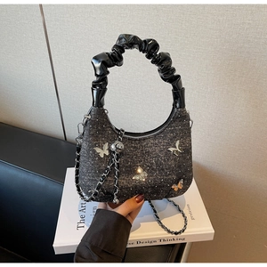 Detail of glitter handbag featuring silver butterfly ornament and patent leather handle