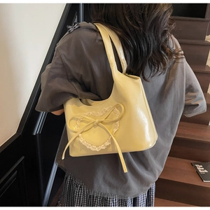 Dettaglio borsa a spalla color crema con toppa a cuore in pizzo e fiocco decorativo