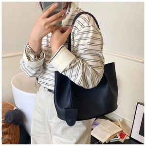 Close-up of a black lychee-grain leather tote bag styled with a casual striped shirt