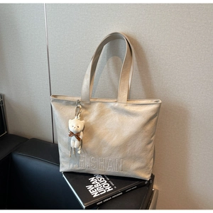 Detail of beige tote bag with H.SHAN embossing and a cute white teddy bear charm