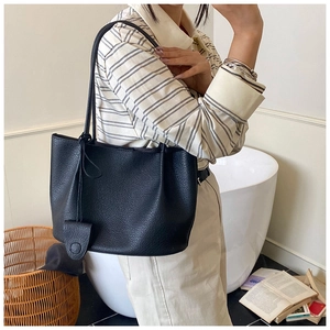 Detail of large black pebble leather tote bag shown on shoulder in a minimalist setting