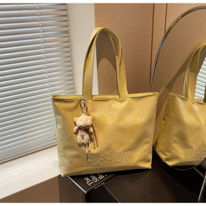 Detail of yellow lychee leather tote with H.SHAN embossing and plush bear charm