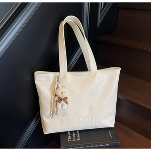 Detail of white PU leather tote with H.SHAN logo and cute plush bear charm on books