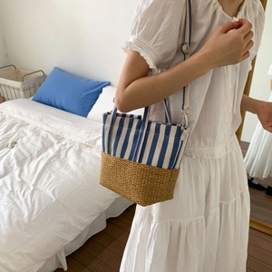 Blue striped canvas and straw woven tote bag shown in a minimalist bedroom setting