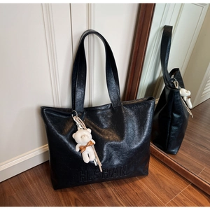 Detail of black wrinkled texture tote bag featuring H.SHAN logo and white teddy bear charm