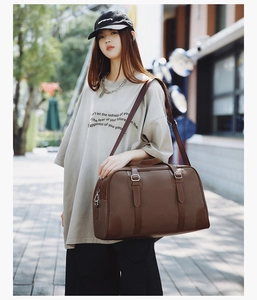 Brown vintage travel bag with silver metal buckles and adjustable shoulder strap worn by model
