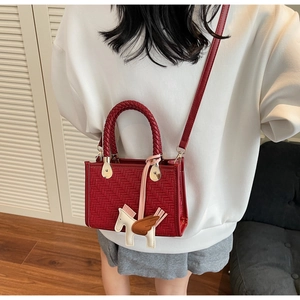 Détail du sac boîte rouge tissé avec poignée tressée et breloque cheval sur un mannequin