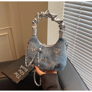 Detail of light blue denim crescent bag with butterfly charm and silver pleated handle