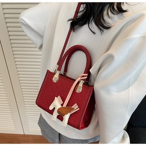 Vue de dessus d'un sac cabas tissé rouge avec charm pégase sur fond à persiennes blanc
