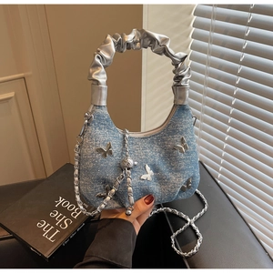 Detail of denim shoulder bag with silver butterfly ornament and wrinkled leather handle