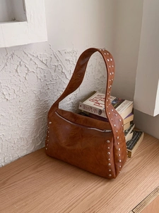 Braune Vintage-Schultertasche mit silbernen Nieten auf einem Holztisch präsentiert