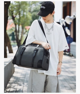 Detail of a large gray and black travel duffel bag with leather trim worn on shoulder