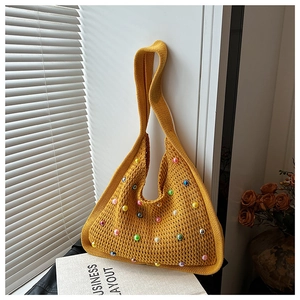 Close-up of yellow knitted hobo bag with colorful pearl accents on a window sill