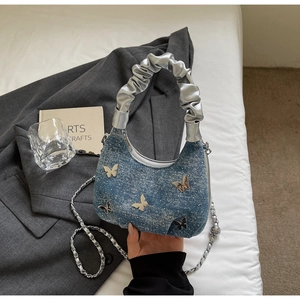 Detail of blue denim hobo bag with metal butterfly ornaments and silver pleated handle