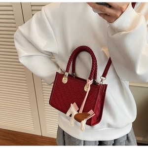 Détail d'un sac bandoulière tressé bordeaux avec un charm de cheval blanc en selfie