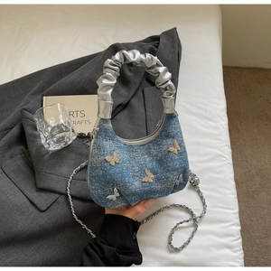 Close-up of denim shoulder bag featuring silver butterfly studs and ruffled handle