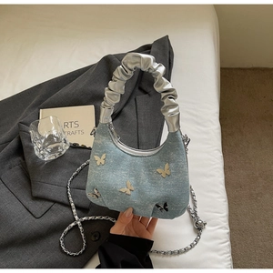 Close-up of light blue denim hobo bag featuring metal butterfly and silver cloud handle