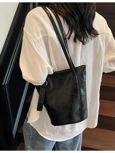 Fashionable black crocodile pattern bucket bag with double straps worn by a model