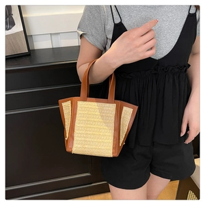 Close-up of woven straw tote bag with brown leather handles held by a model
