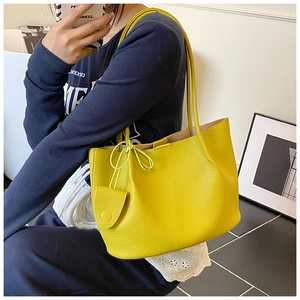 Detailed view of yellow faux leather tote bag with side bow and charm detail