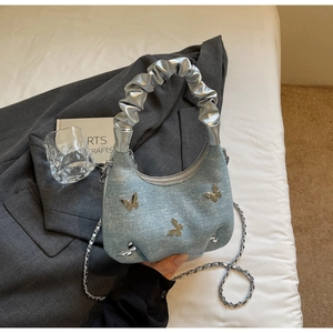 Detailed shot of light blue denim half-moon bag with silver butterfly charms and chain strap