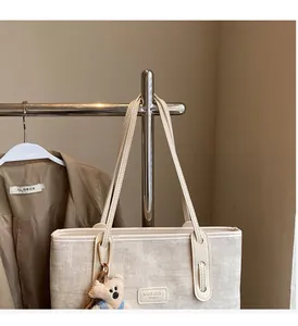 Detail of light beige woven canvas tote bag featuring leather logo and plush bear charm