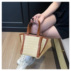 Detail of a straw tote bag with brown leather trim and handles in a cozy indoor setting