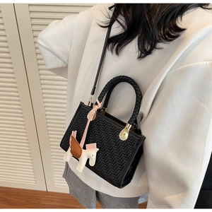 Détail d'un sac à main noir tressé avec poignées rondes et breloque cheval décorative