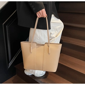 Gros plan d'un cabas beige texturé porté par un mannequin sur un escalier en bois