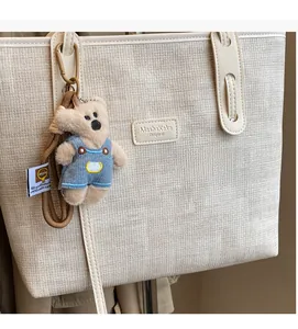 Detail of off-white woven tote bag featuring leather logo tag and cute blue bear charm