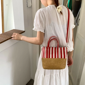 Close-up of small straw tote bag with red stripes and adjustable crossbody strap