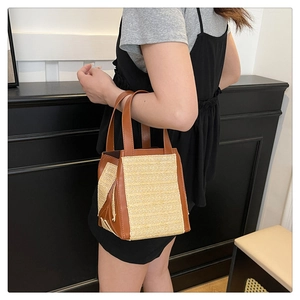 Detail of hand-woven straw tote bag featuring brown faux leather trim and sturdy handles
