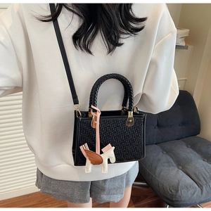 Détail d'un sac à main noir tressé avec un charm Pégase et des ferrures dorées