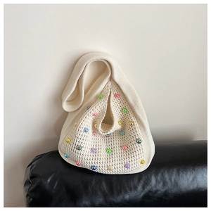 Detail of a beige knit beach bag featuring colorful faux pearls on a woven texture