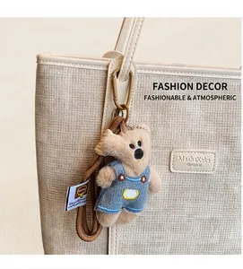 Close-up of a plush bear charm with denim overalls attached to a beige textured tote bag