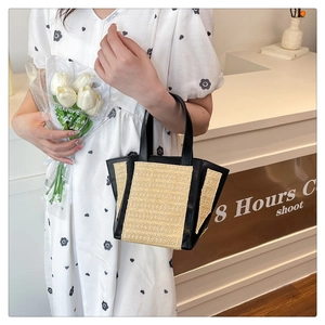 Detail of straw woven tote bag featuring black PU leather trim and handle texture