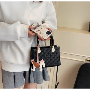 Détail du sac à main noir tressé avec breloque pégase et poignées rondes élégantes