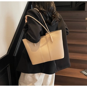 Détail de la texture cuir litchi beige du sac porté sur une veste de blazer noire