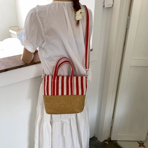 Detail view of red and white striped straw tote bag worn by a model in bright setting