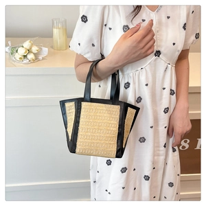Detailed close-up of summer woven straw tote bag with black leather handles and side trim