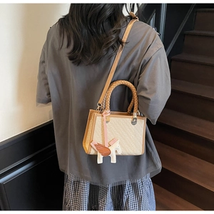 Détail du sac à main tissé crème avec bordure marron et breloque pégase