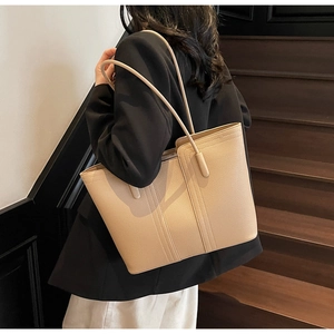 Détail d'un grand sac cabas beige avec texture litchi porté à l'épaule par un modèle